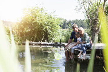 Glückliche Familie sitzt mit einem Kescher auf einem Steg an einem See - RBF001961
