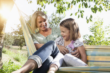 Happy mother and daughter sitting in hammock - RBF001964