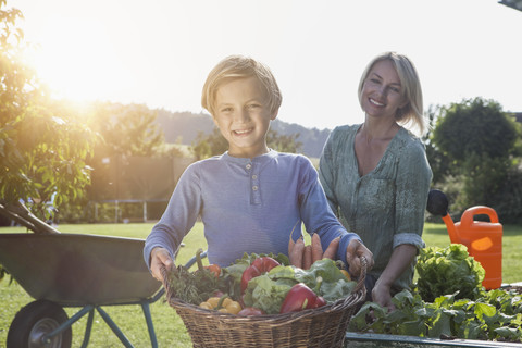 Junge mit Mutter im Garten, der einen Korb mit Gemüse trägt, lizenzfreies Stockfoto