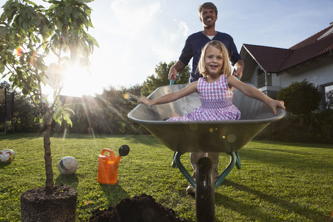 Father with daughter in wheelbarrow planting tree in garden stock photo