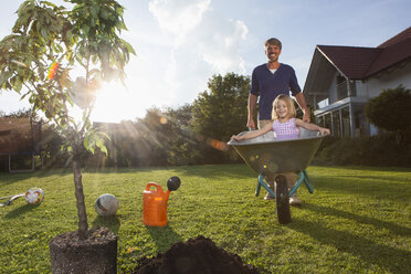 Vater mit Tochter in Schubkarre pflanzt Baum im Garten - RBF002022