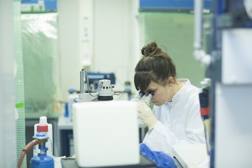 Junge Naturwissenschaftlerin schaut durch ein Mikroskop im Laboratorium - SGF001109