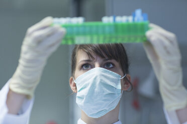 Junge Naturwissenschaftlerin mit Maske und Schutzhandschuhen bei der Arbeit im Laboratorium - SGF001110