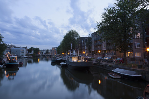 Niederlande, Amsterdam, Blick auf Boote am Stadtkanal und Mehrfamilienhaus im Hintergrund, lizenzfreies Stockfoto