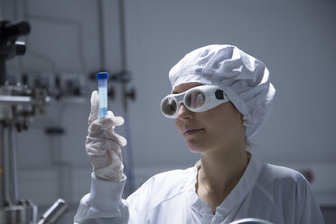 Young female technician with protective cap and safety glasses watching a tube in a labroratory - SGF001118