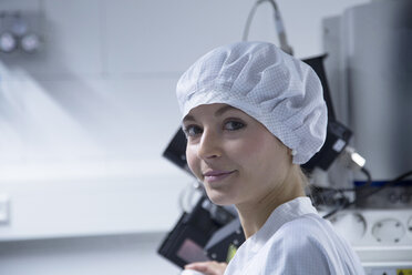 Porträt einer lächelnden jungen Technikerin mit Schutzkappe in einem Laboratorium - SGF001121