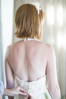 Brautjungfer knöpft Hochzeitskleid der Braut zu - ZEF002788