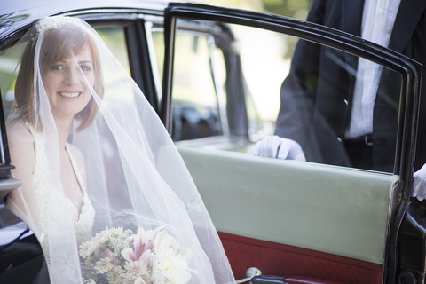 Lächelnde Braut beim Aussteigen aus dem Auto vor ihrer Hochzeit, lizenzfreies Stockfoto