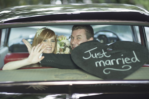 Glückliches Brautpaar winkt nach der Hochzeit im Auto, lizenzfreies Stockfoto