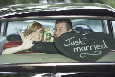 Glückliches Brautpaar winkt nach der Hochzeit im Auto - ZEF002580