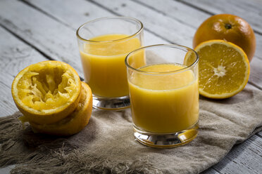 Zwei Gläser mit frisch gepresstem Orangensaft und Orangen auf Stoff und Holz - SARF001070