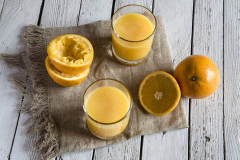 Zwei Gläser mit frisch gepresstem Orangensaft und Orangen auf Stoff und Holz, lizenzfreies Stockfoto