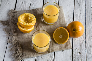 Zwei Gläser mit frisch gepresstem Orangensaft und Orangen auf Stoff und Holz - SARF001072