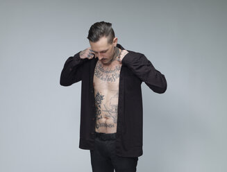 Man with tattoo on his waist up dressing black shirt in front of grey background - RH000394