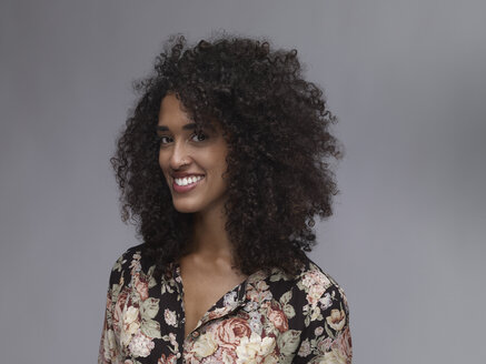 Porträt einer lächelnden jungen Frau mit Nasenring und Afro vor einem grauen Hintergrund - RH000399