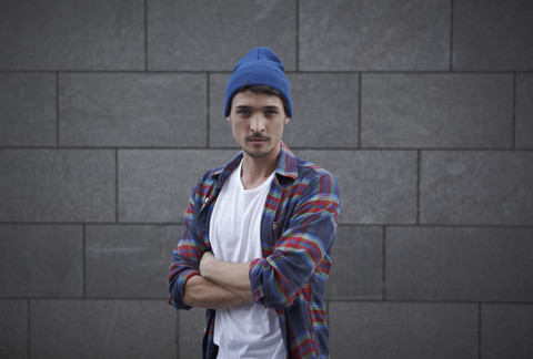 Porträt eines jungen Mannes mit verschränkten Armen und blauer Mütze, lizenzfreies Stockfoto