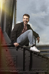 Portrait of laughing man sitting on bridge pier - RHF000405