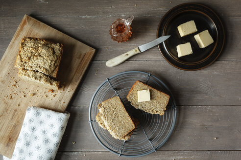 Scheiben selbstgebackenes glutenfreies Buchweizenbrot, Butterstückchen und Glasdose mit Honig auf Holz - EVGF001019