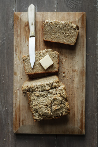Selbstgebackenes glutenfreies Buchweizenbrot, ein Stück Butter und ein Holzbrett mit Küchenmesser, lizenzfreies Stockfoto