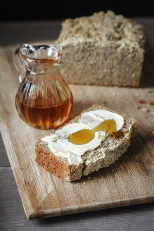 Eine Scheibe selbstgebackenes Buchweizenbrot mit Butter und Honig auf einem Holzbrett - EVGF001027