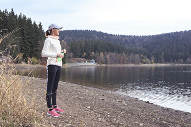 Weibliche Joggerin mit Wasserflasche steht am Seeufer und genießt die Aussicht - VTF000357