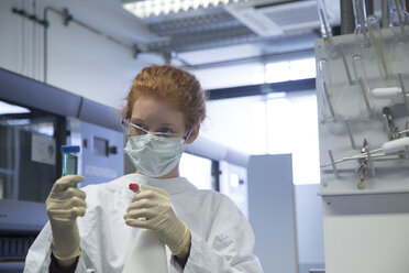 Junge Naturwissenschaftlerin mit Maske beim Desinfizieren eines Tests im biochemischen Labor - SGF001164