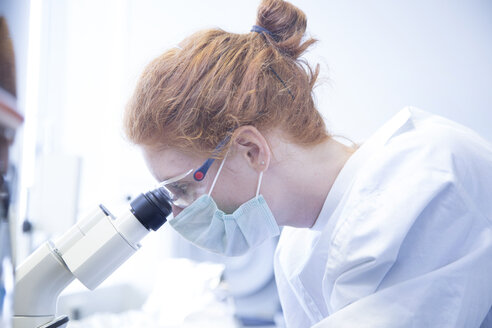 Young female natural scientist looking through microscope in biochemistry laboratory - SGF001128