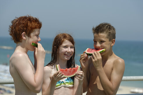 Italien, Mädchen und zwei Jungen im Teenageralter essen Wassermelonenscheiben am Strand - LBF000996