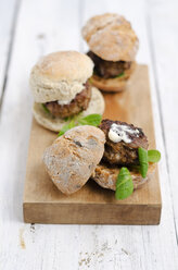 Three garnished bread rolls with patty and lamb's lettuce on wooden board and table - ODF000888