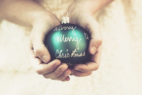 Girl's hands holding green Christmas bauble with the words 'Merry Christmas' stock photo