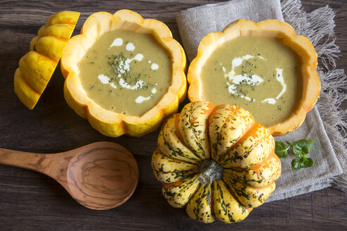 Kürbiscremesuppe in ausgehöhlten Chamäleonkürbissen auf Stoff und dunklem Holz - SARF001091