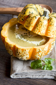 Kürbiscremesuppe in ausgehöhltem Chamäleonkürbis auf Stoff und dunklem Holz - SARF001092