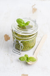 Preserving jar of fresh pesto, wooden spoon and basil leaves on white wood - ODF000901