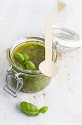 Preserving jar of fresh pesto, wooden spoon and basil leaves on white wood - ODF000902