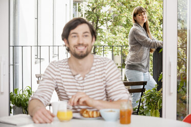 Man having breakfast with woman standing on balcony - FMKF001367