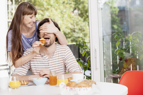 Woman feeding man at breakfast table - FMKF001370