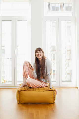 Relaxed woman with cell phone on ottoman at home stock photo