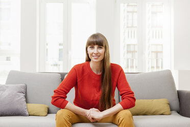 Smiling woman sitting on sofa - FMKF001385