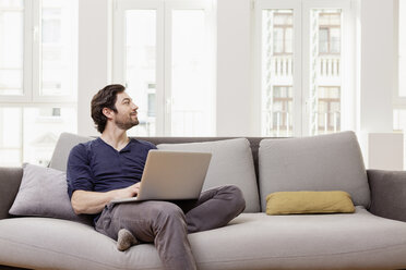 Man sitting on couch using laptop - FMKF001388