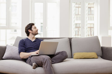 Mann sitzt auf der Couch und benutzt einen Laptop - FMKF001388