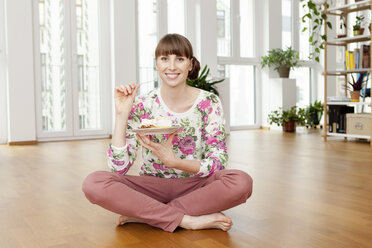 Lächelnde Frau sitzt auf dem Boden und genießt ein Stück Kuchen - FMKF001405