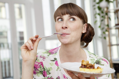 Lächelnde Frau genießt ein Stück Kuchen, lizenzfreies Stockfoto