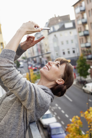 Lächelnd auf dem Balkon lehnt sich die Frau zurück und macht ein Selfie, lizenzfreies Stockfoto