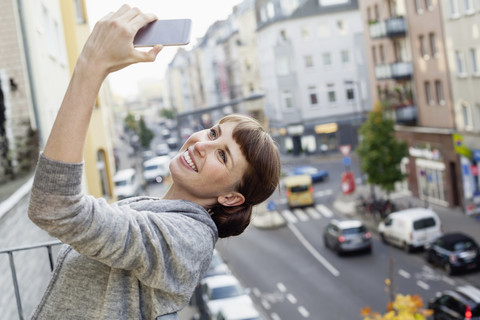 Lächelnd auf dem Balkon lehnt sich die Frau zurück und macht ein Selfie, lizenzfreies Stockfoto