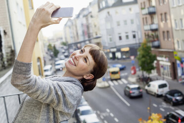 Smiling on balcony leaning back woman taking selfie - FMKF001414