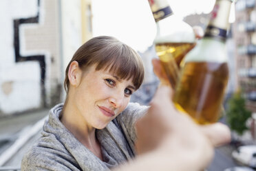 Lächelnde Frau auf dem Balkon, die auf eine Bierflasche anstößt - FMKF001437