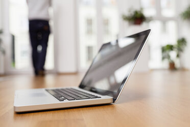 Laptop auf dem Boden mit Mann im Hintergrund - FMKF001438