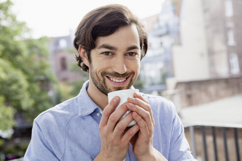 Porträt eines lächelnden Mannes auf einem Balkon, der Kaffee trinkt - FMKF001419