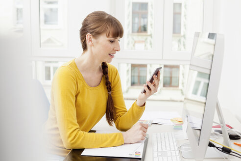 Frau mit Mobiltelefon im Home Office - FMKF001426