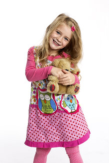 Porträt eines glücklichen kleinen Mädchens mit ihrem Teddybär in einem bunten Kleid vor einem weißen Hintergrund - GDF000618